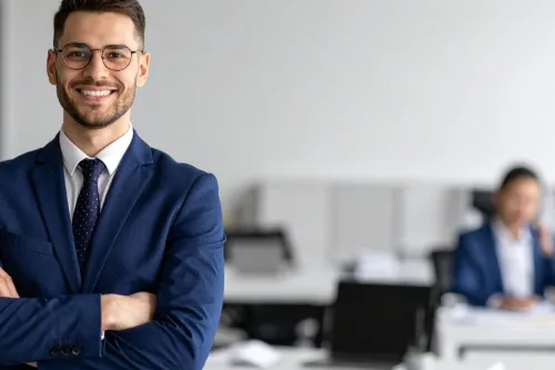 Homem de fato sorridente e braços cruzados num escritório, transmitindo confiança para empreender